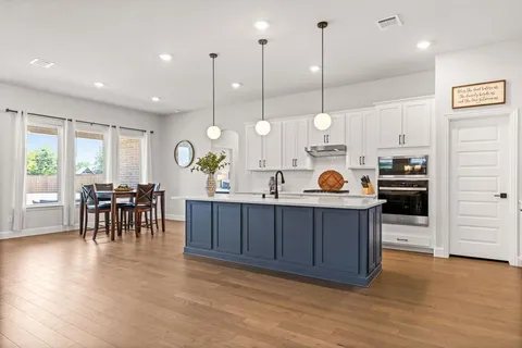 a kitchen with stainless steel appliances granite countertop a stove a sink a dining table and chairs with wooden floor