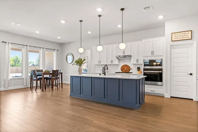 a kitchen with stainless steel appliances granite countertop a stove a sink a dining table and chairs with wooden floor