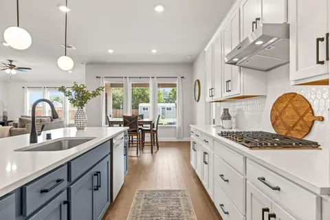 a kitchen with stainless steel appliances granite countertop a stove a sink dishwasher and white cabinets with wooden floor