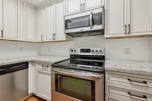 a kitchen with stainless steel appliances granite countertop white cabinets and a stove top oven
