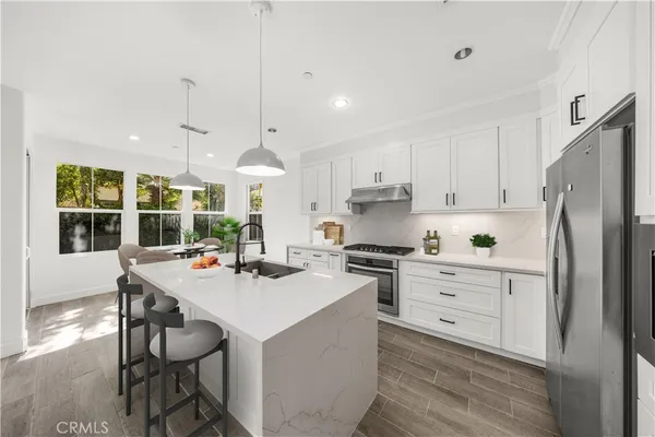 a kitchen with stainless steel appliances a stove a sink dishwasher a refrigerator with white cabinets and wooden floor