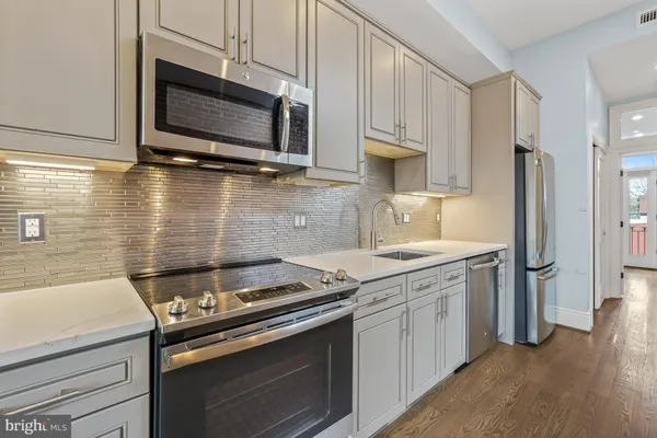 a kitchen with stainless steel appliances granite countertop a sink a stove white cabinets with wooden floor