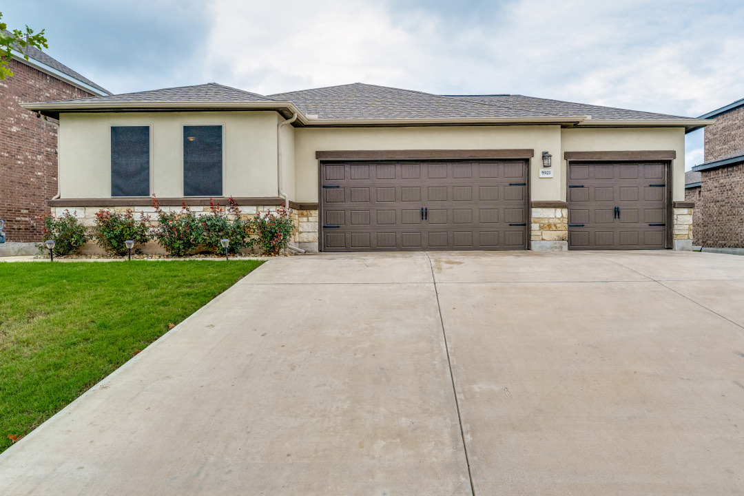 5921 Lehman Way Austin, TX 78747 - Photo 3 of 25 A cream-colored stucco and stone facade welcomes with a spacious concrete driveway leading to two large garage doors.