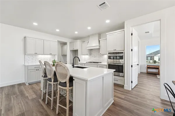 a kitchen with a sink a stove a refrigerator and white cabinets with wooden floor