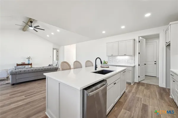 a large white kitchen with a stove a sink a refrigerator and a dining table with wooden floor