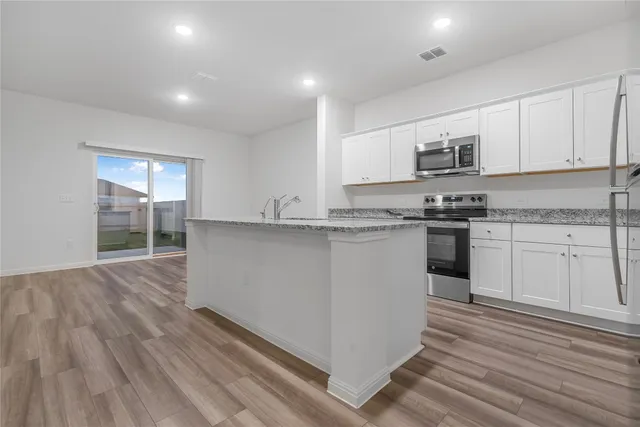 a kitchen with stainless steel appliances granite countertop a stove top oven a sink dishwasher and white cabinets with wooden floor