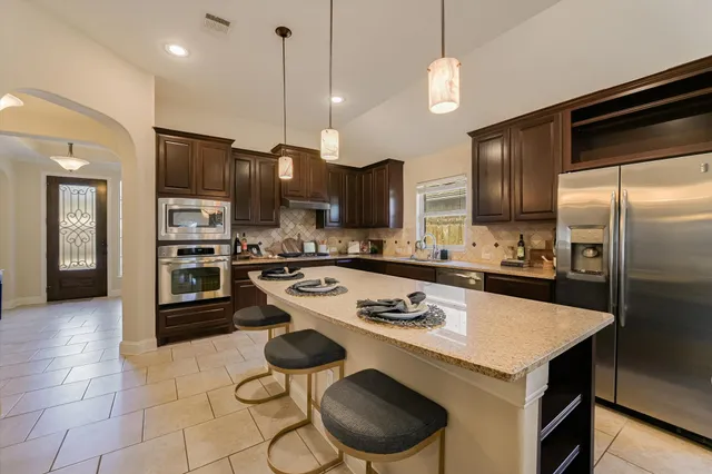 a kitchen with kitchen island stainless steel appliances a stove a sink a refrigerator cabinets and chairs
