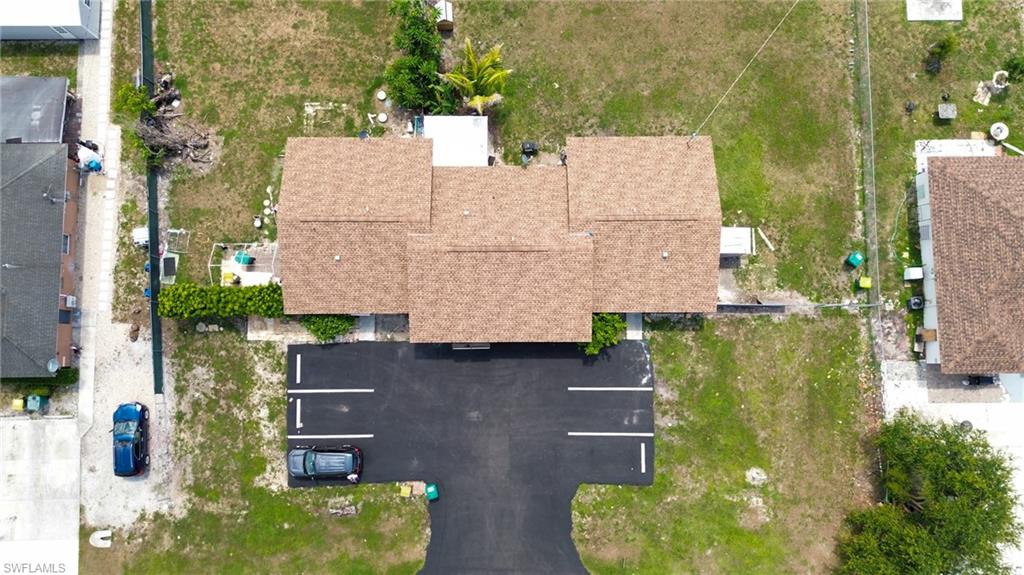 1940 48th Street Southwest Naples, FL 34116 - Photo 11 of 33 Property featuring a brown shingle roof, paved parking area with marked spaces, and a landscaped hedge