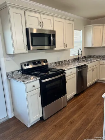 a kitchen with granite countertop a stove top oven a sink dishwasher and white cabinets with wooden floor