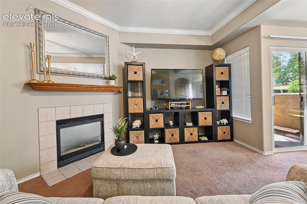 3715 Riviera Grove, Unit 101 Colorado Springs, CO 80922 - Photo 12 of 36 Living area featuring a tiled fireplace with a wood mantle, crown molding, and neutral wall paint