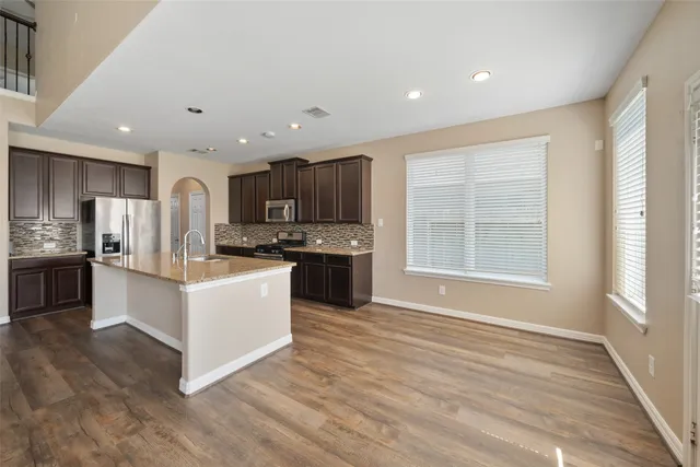 a kitchen with granite countertop a stove top oven a sink a refrigerator and white cabinets with wooden floor