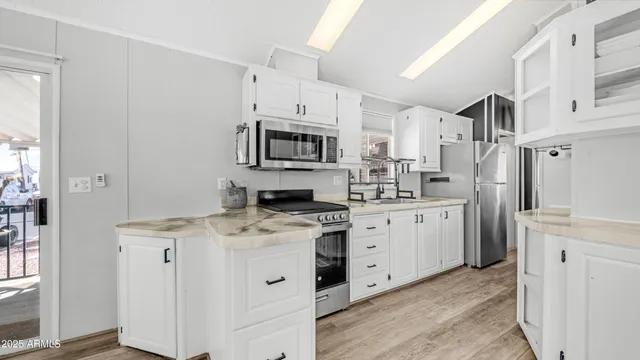 a kitchen with stainless steel appliances granite countertop a refrigerator a stove top oven a sink dishwasher and white cabinets with wooden floor