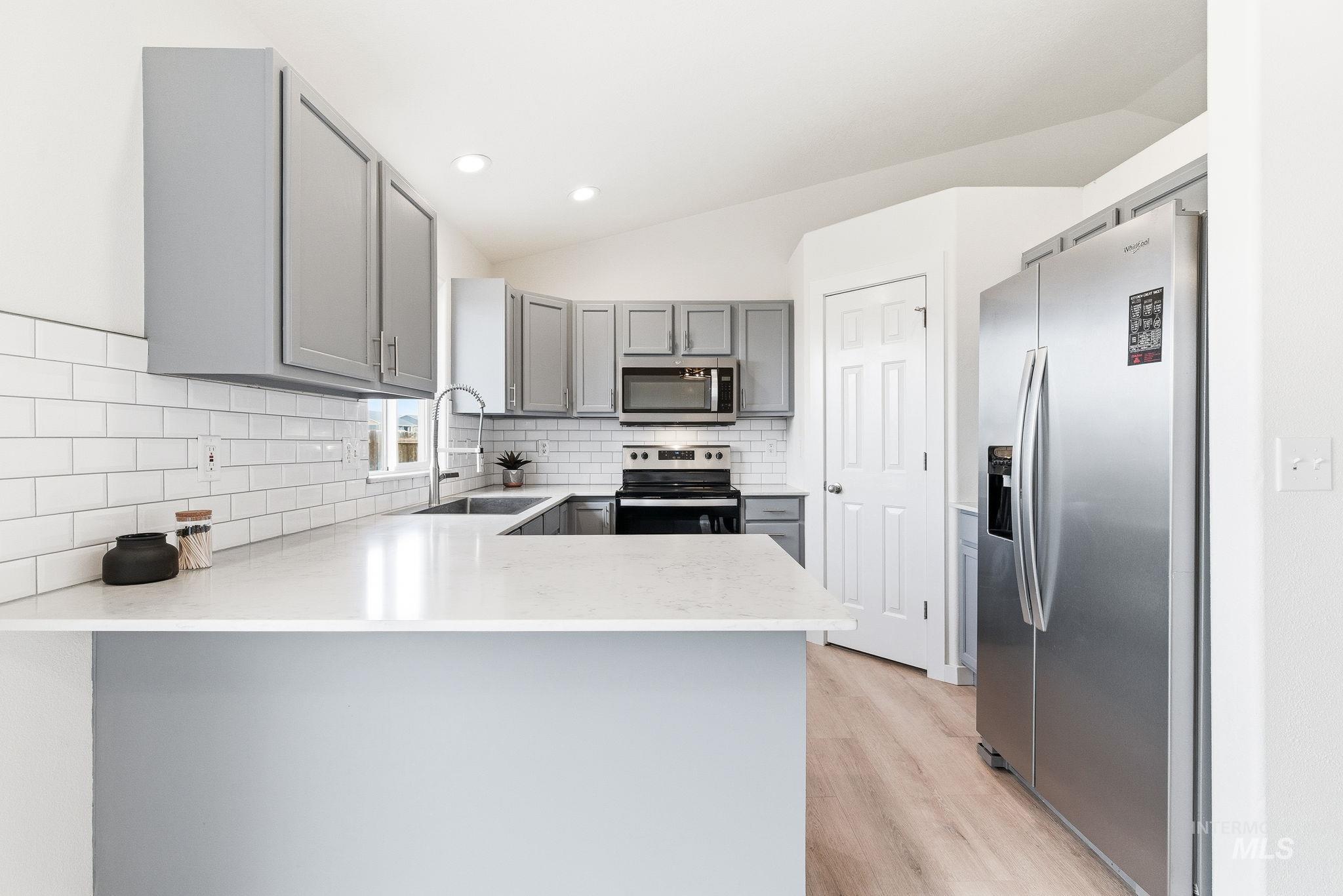 696 West Rams Hill Street Kuna, ID 83634 - Photo 14 of 46 Kitchen featuring gray cabinets, stainless steel appliances, a peninsula, vaulted ceiling, and light wood-style floors