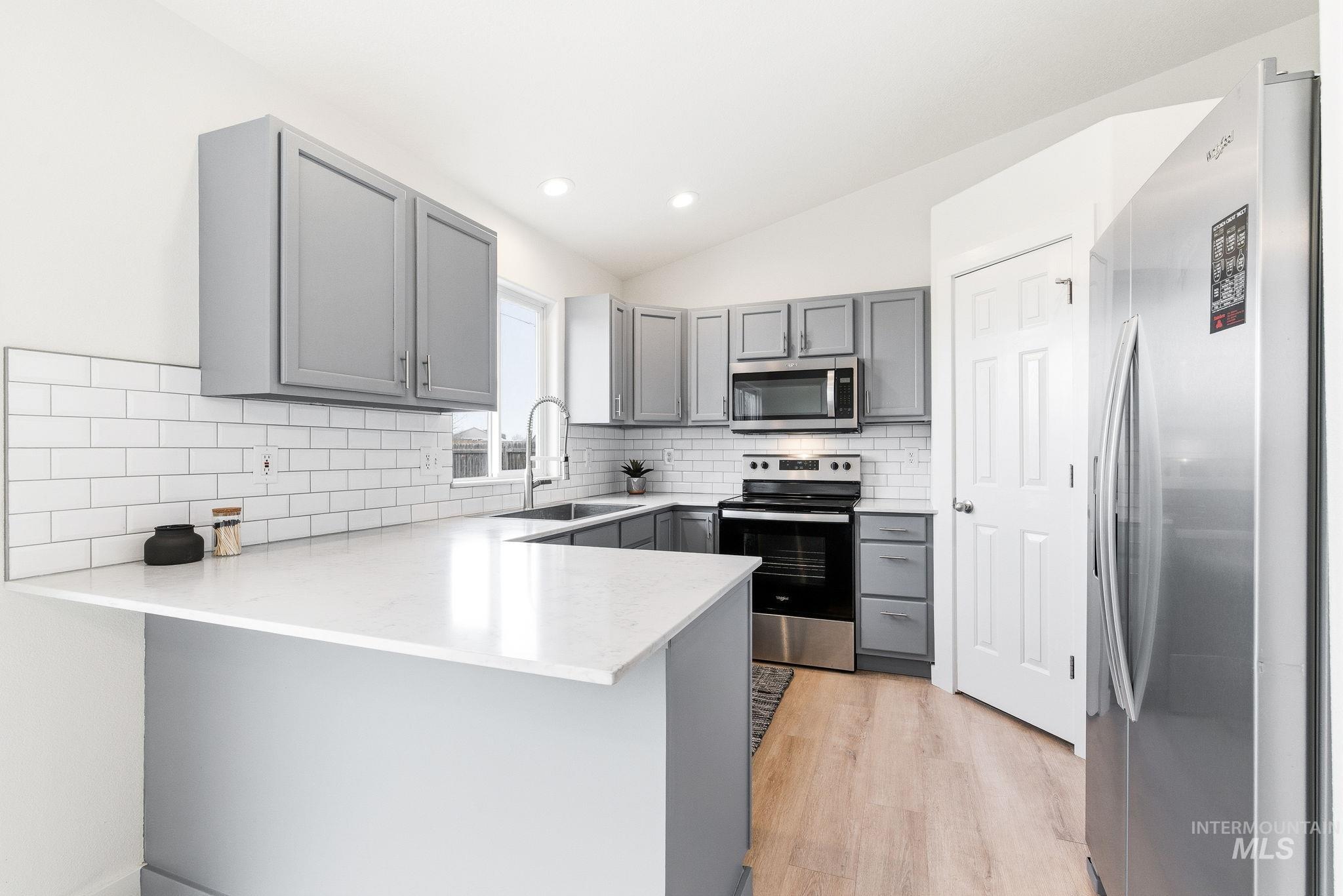 696 West Rams Hill Street Kuna, ID 83634 - Photo 15 of 46 Kitchen featuring gray cabinetry, stainless steel appliances, a peninsula, light wood-type flooring, and light stone countertops