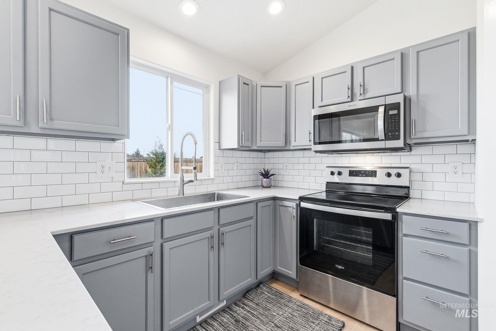696 West Rams Hill Street Kuna, ID 83634 - Photo 16 of 46 Kitchen featuring gray cabinetry, stainless steel appliances, lofted ceiling, light stone countertops, and recessed lighting