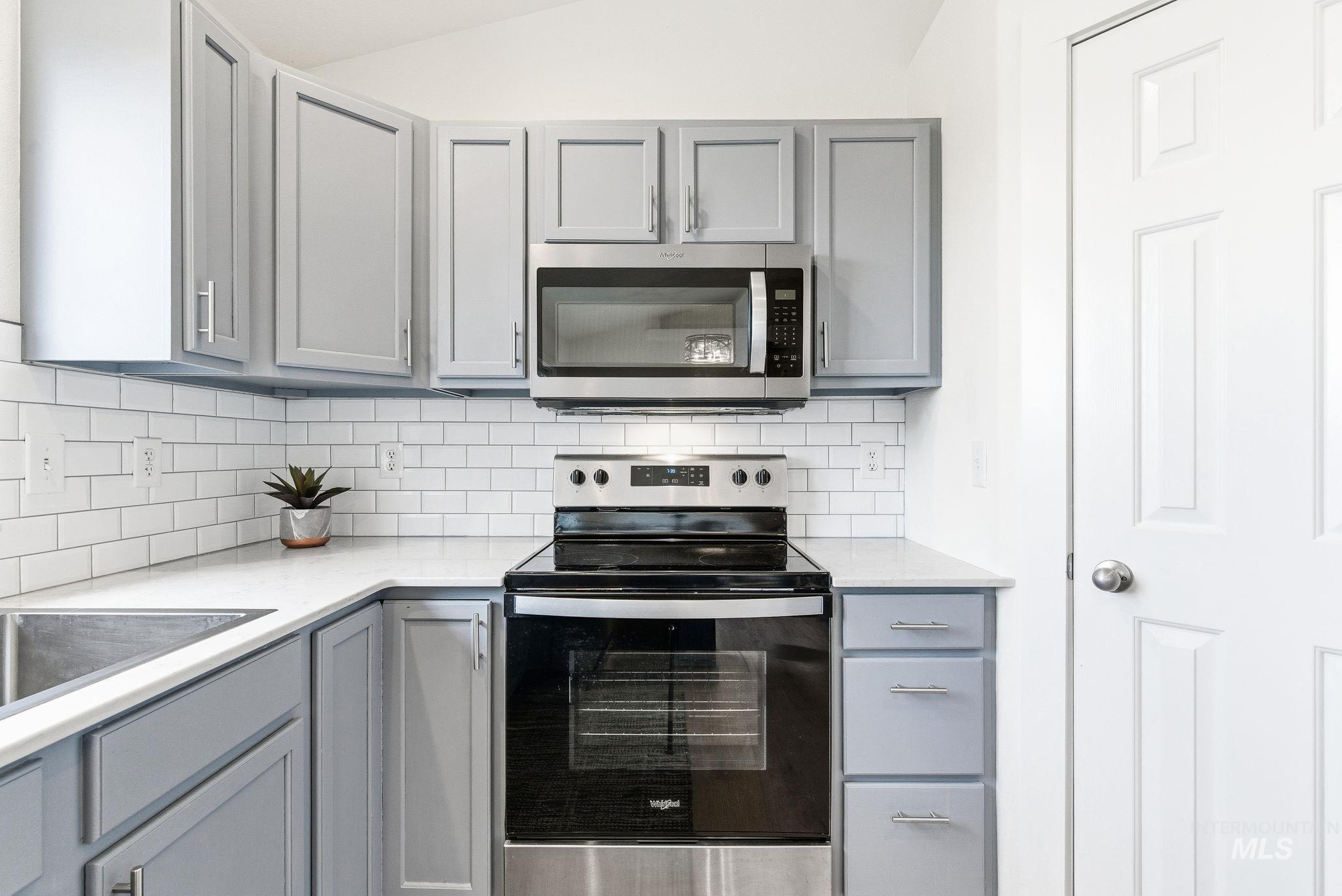 696 West Rams Hill Street Kuna, ID 83634 - Photo 19 of 46 Kitchen with gray cabinets, stainless steel appliances, light stone counters, decorative backsplash, and vaulted ceiling