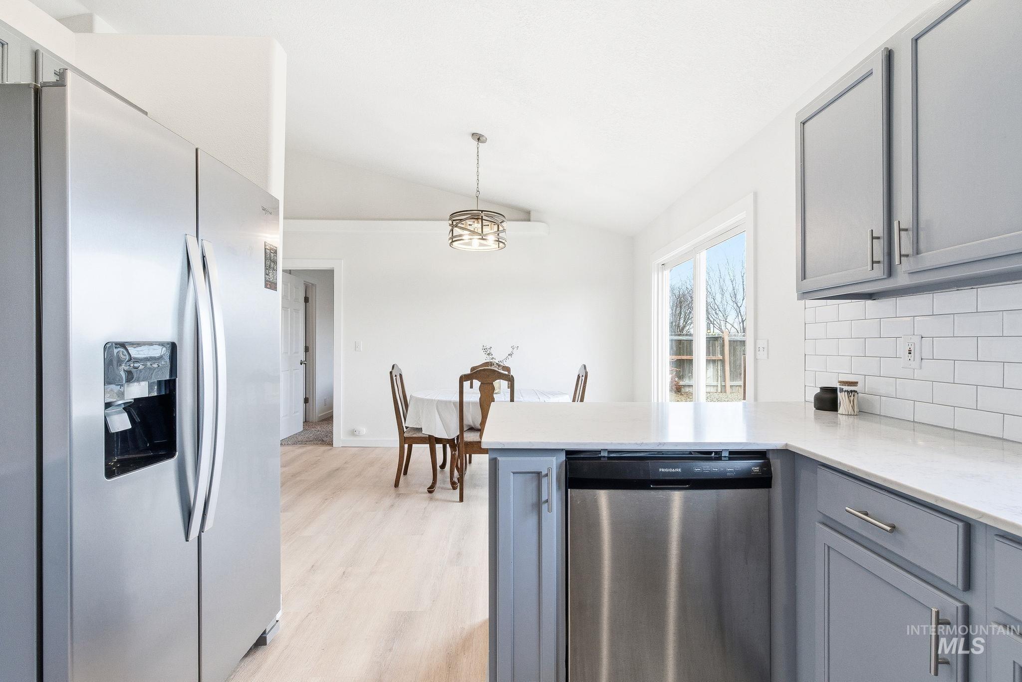 696 West Rams Hill Street Kuna, ID 83634 - Photo 21 of 46 Kitchen with stainless steel appliances, gray cabinetry, vaulted ceiling, backsplash, and light wood-type flooring