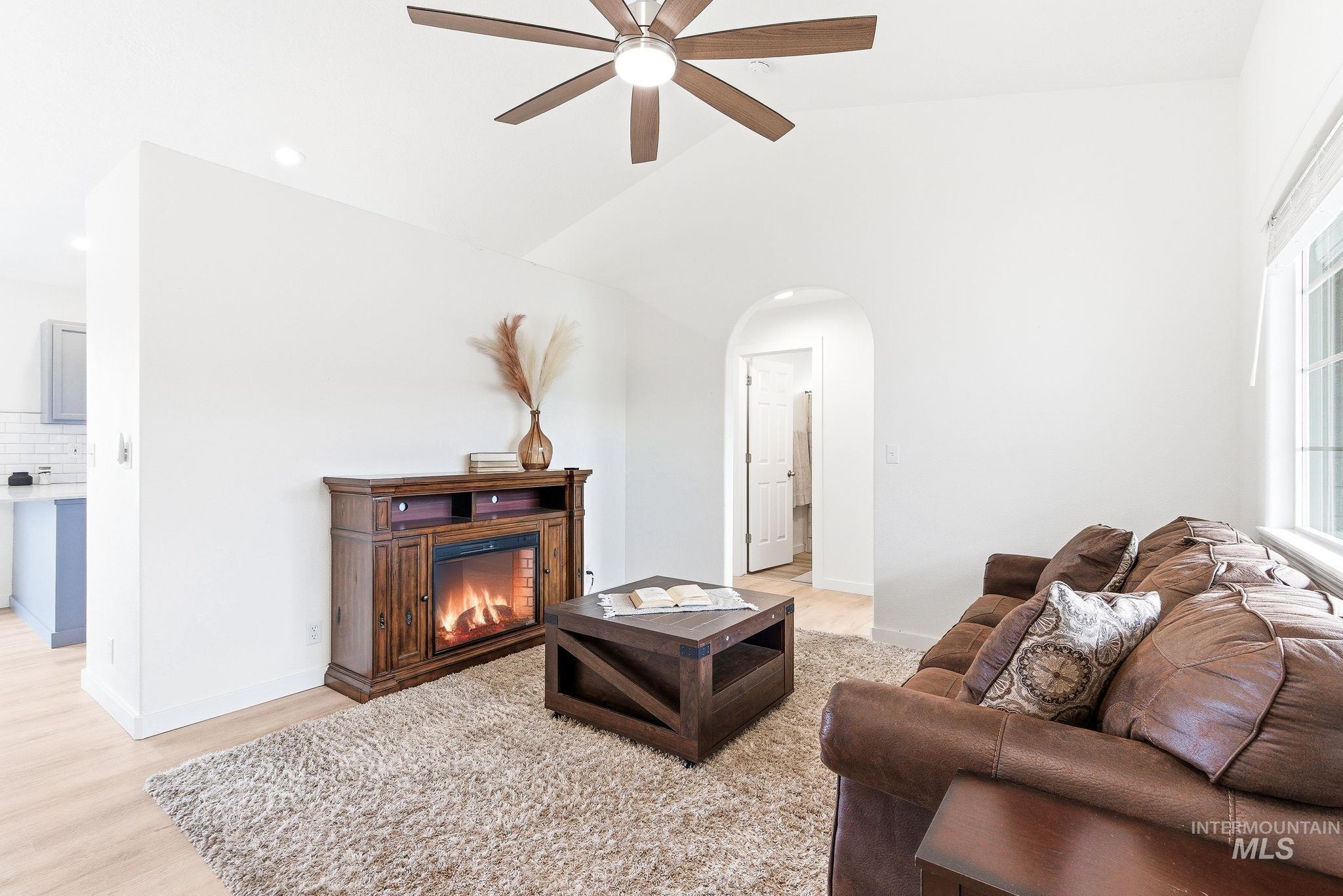 696 West Rams Hill Street Kuna, ID 83634 - Photo 5 of 46 Living room featuring arched walkways, lofted ceiling, light wood-type flooring, a glass covered fireplace, and ceiling fan