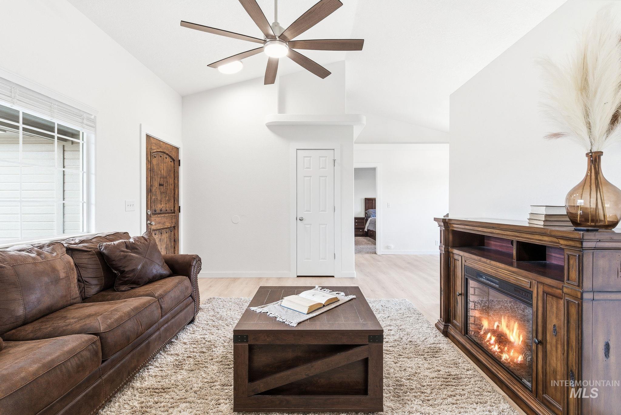 696 West Rams Hill Street Kuna, ID 83634 - Photo 8 of 46 Living area featuring light wood-style floors, a glass covered fireplace, a ceiling fan, and vaulted ceiling
