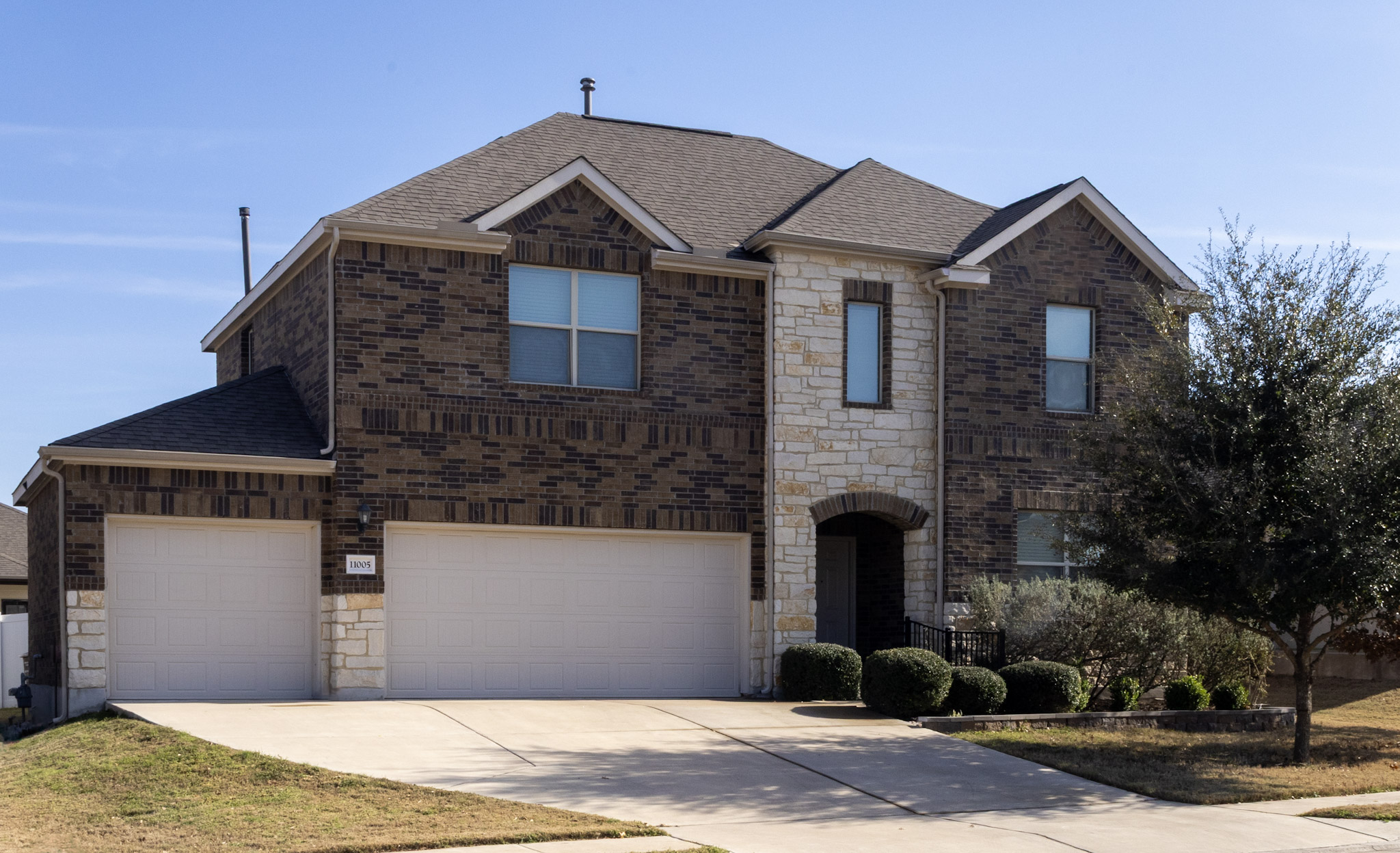 View of front of property with stone siding, a shingled roof, driveway, and brick siding