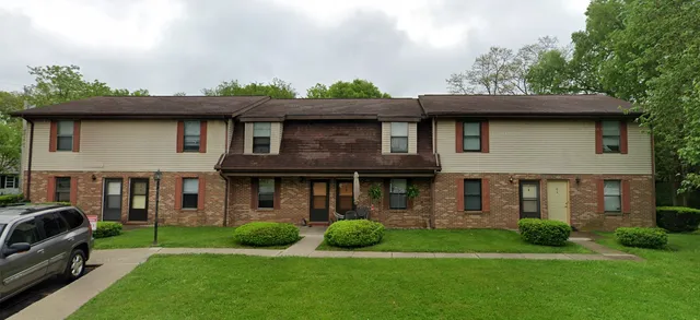a brick house with a yard plants and large trees