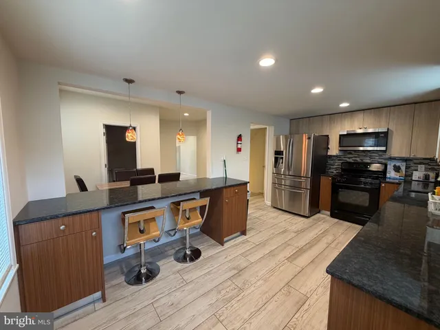 a kitchen with stainless steel appliances kitchen island granite countertop a refrigerator a stove and a sink with wooden floor