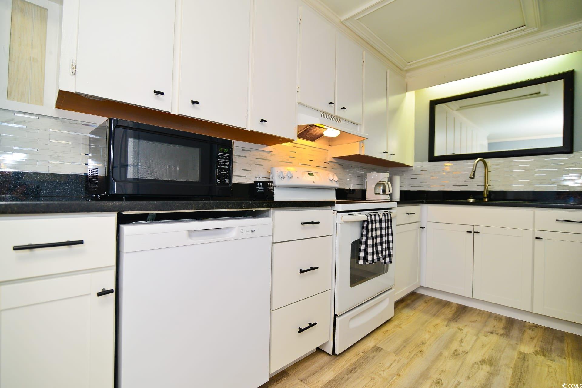 219 27th Avenue North North Myrtle Beach, SC 29582 - Photo 6 of 34 Kitchen featuring dark countertops, white appliances, under cabinet range hood, white cabinets, and tasteful backsplash