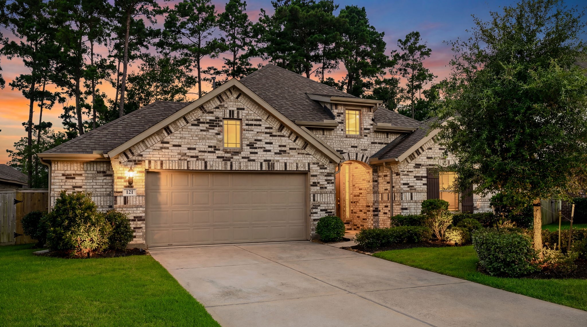 This charming home features a brick exterior with a welcoming archway entrance. It includes a two-car garage and well-maintained landscaping with shrubs. The design is classic and appealing, offering great curb appeal.