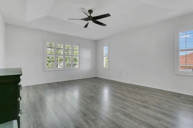 an empty room with wooden floor fan and windows