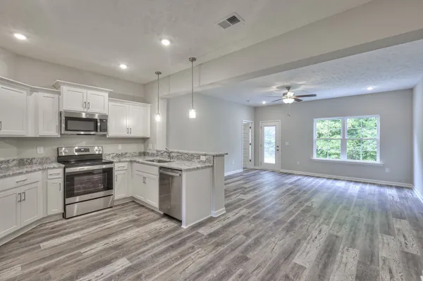 a large kitchen with kitchen island granite countertop a stove top oven a sink dishwasher and white cabinets with wooden floor