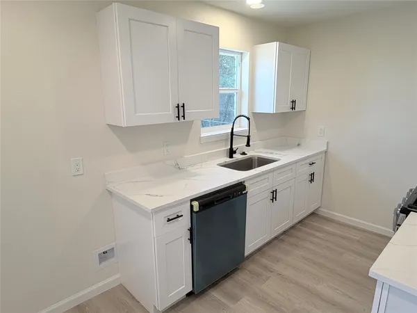 a kitchen with a sink dishwasher and white cabinets with wooden floor