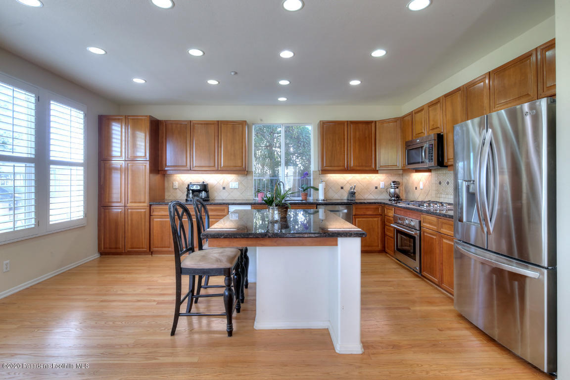 7461 Chanteclair Court Tujunga, CA 91042 - Photo 10 of 44 a kitchen with granite countertop a refrigerator a stove top oven and a dining table with wooden floor