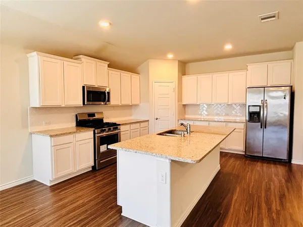 a kitchen with stainless steel appliances granite countertop a sink a stove a refrigerator with white cabinets and wooden floor
