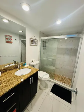 a bathroom with a granite countertop sink a toilet a mirror and shower