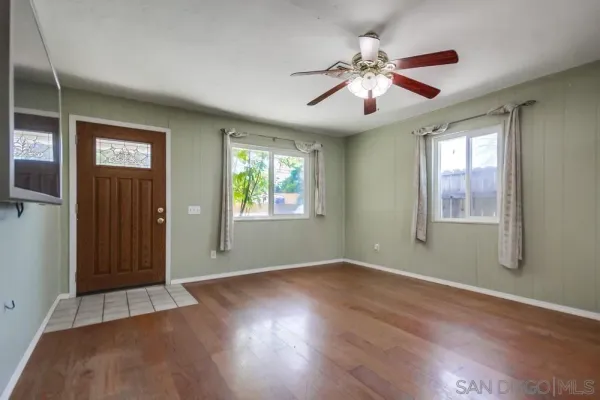 an empty room with wooden floor chandelier fan and windows