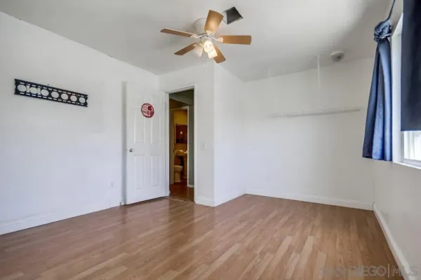 a view of an empty room with wooden floor and a chandelier fan