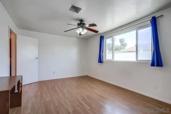 a view of an empty room with wooden floor and a ceiling fan