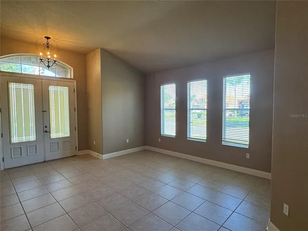 an empty room with chandelier fan and windows