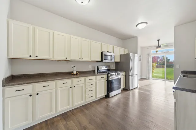 a kitchen with stainless steel appliances granite countertop a stove top oven a sink a refrigerator white cabinets and wooden floor