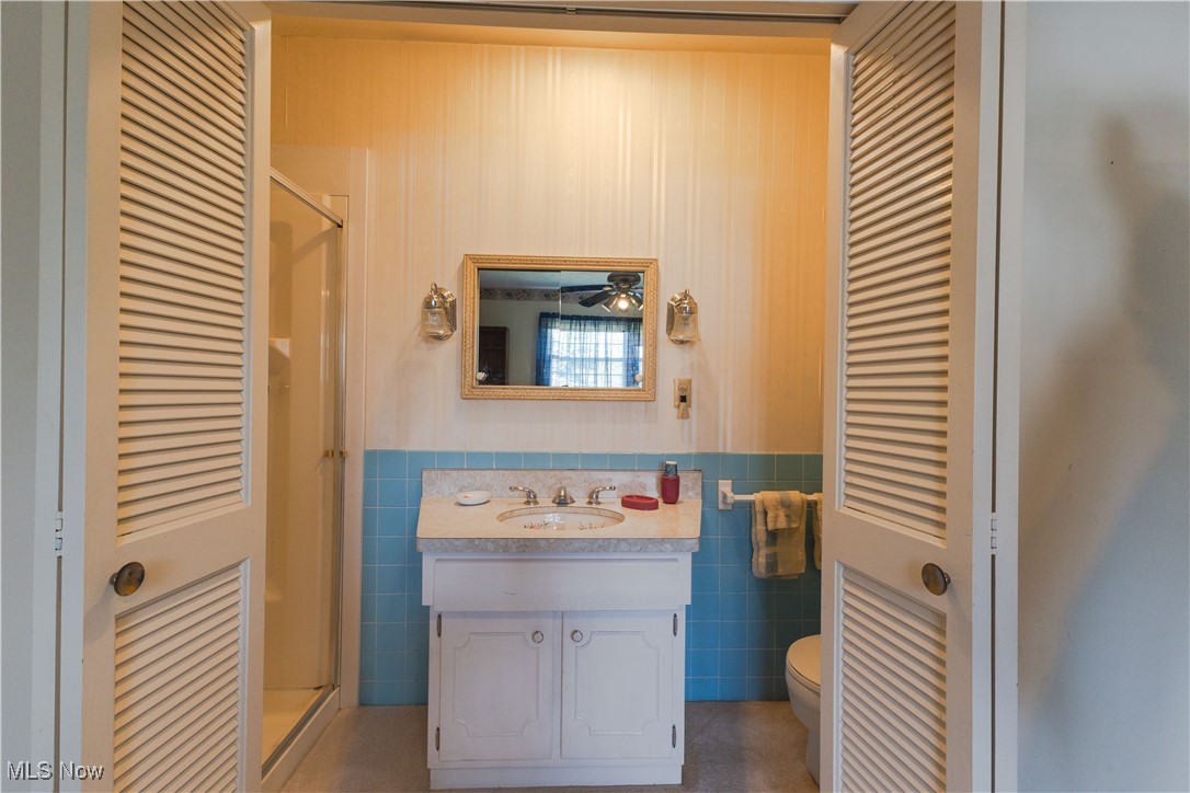 1639 South Ridge Road West Ashtabula, OH 44004 - Photo 27 of 44 Full bath featuring vanity, a stall shower, toilet, a wainscoted wall, and tile walls