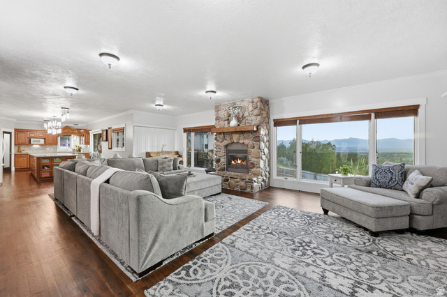 2342 Charros Road Sandy, UT 84092 - Photo 14 of 94 Spacious living area featuring rich wood-finish flooring, a stone-clad fireplace with a natural wood mantel, and large picture windows showcasing distant mountains