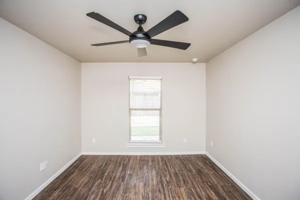 an empty room with wooden floor ceiling fan and windows