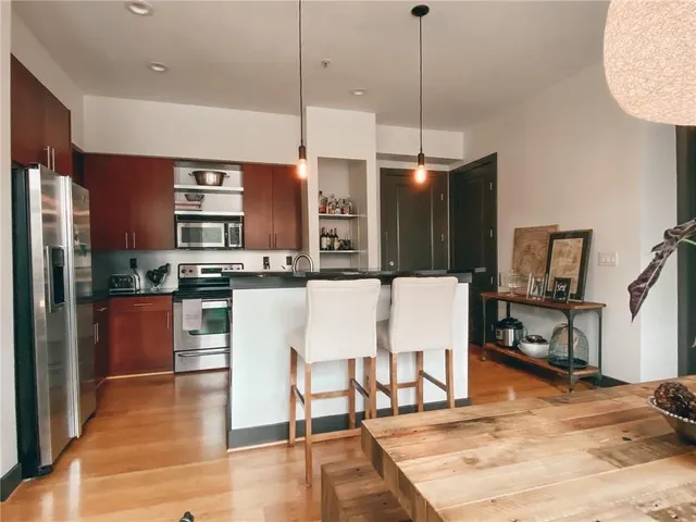 a kitchen with stainless steel appliances kitchen island granite countertop a refrigerator a stove a sink and a dining table with wooden floor