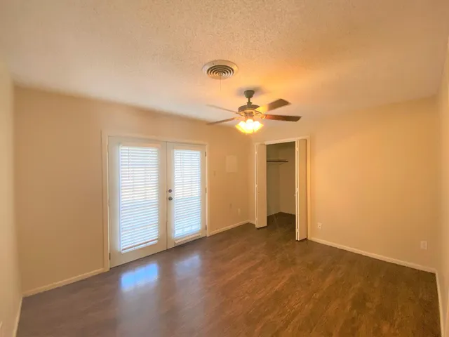a view of an empty room with wooden floor and a ceiling fan