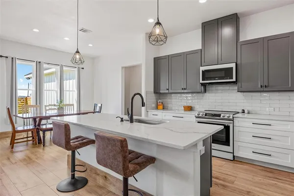 a kitchen with stainless steel appliances granite countertop a stove a refrigerator a sink a dining table and chairs with wooden floor