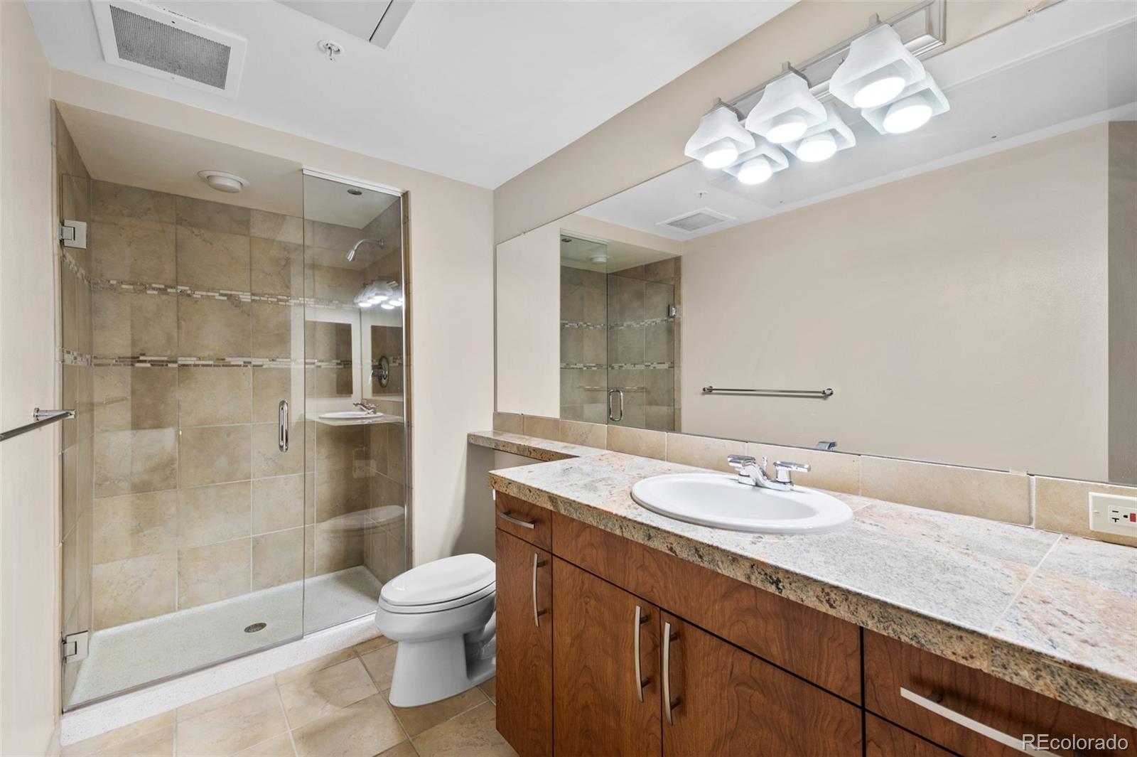 8100 East Union Avenue, Unit 814 Denver, CO 80237 - Photo 28 of 38 a bathroom with a granite countertop sink a toilet a mirror and shower
