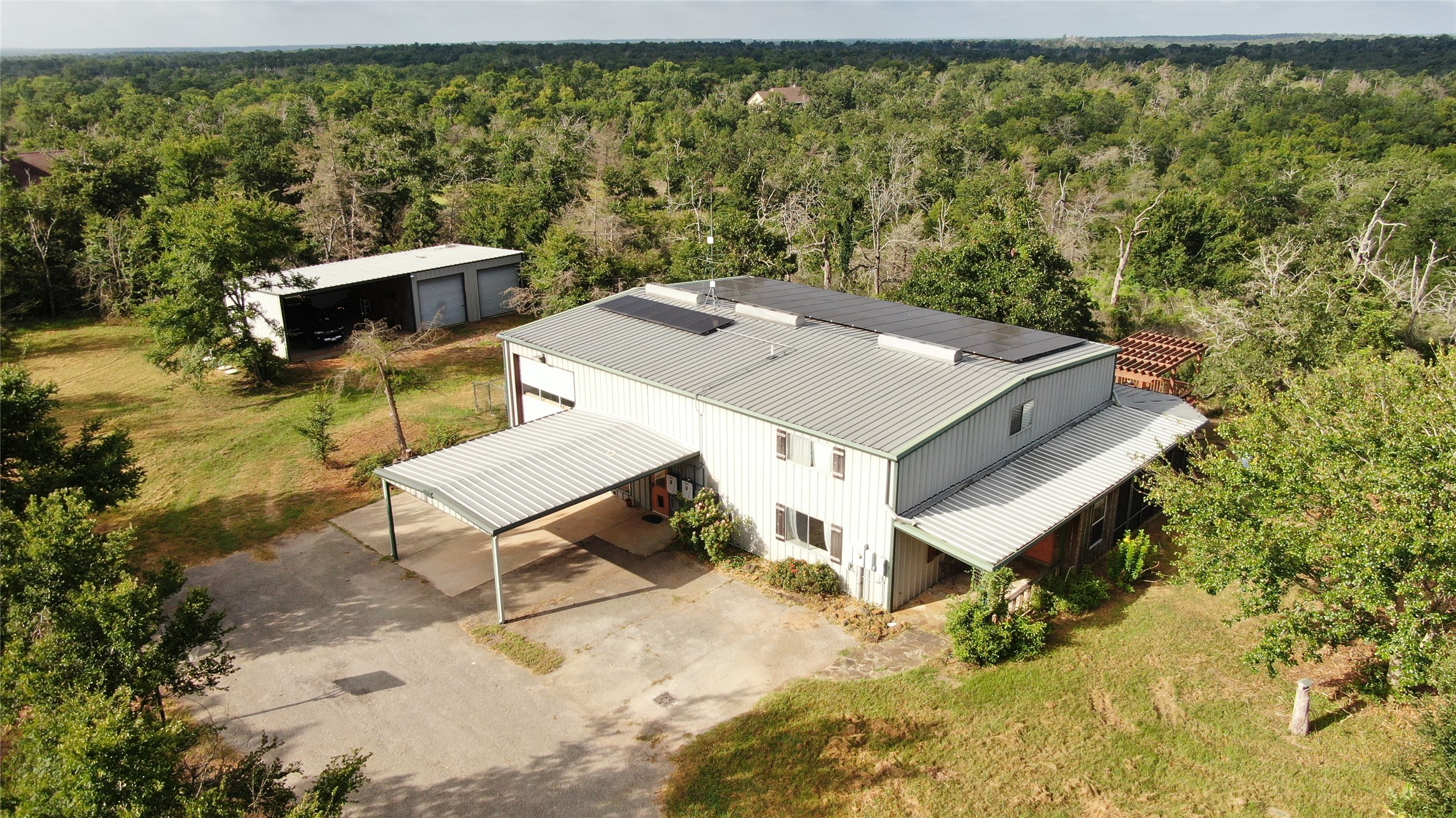 1004 22 Hills Road Gause, TX 77857 - Photo 21 of 37 A spacious barn-style dwelling with a metal roof and solar panels, nestled in a lush, wooded setting.