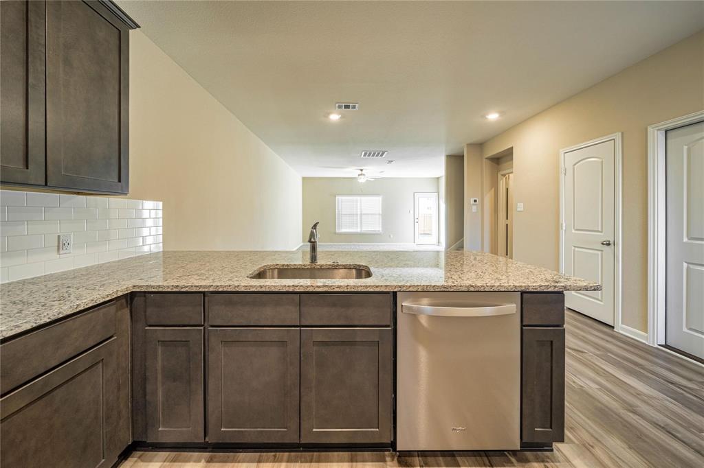 274 Honeysuckle Lane Princeton, TX 75407 - Photo 3 of 35 Kitchen with dark brown cabinetry, stainless steel dishwasher, light stone countertops, a peninsula, and light wood-style flooring