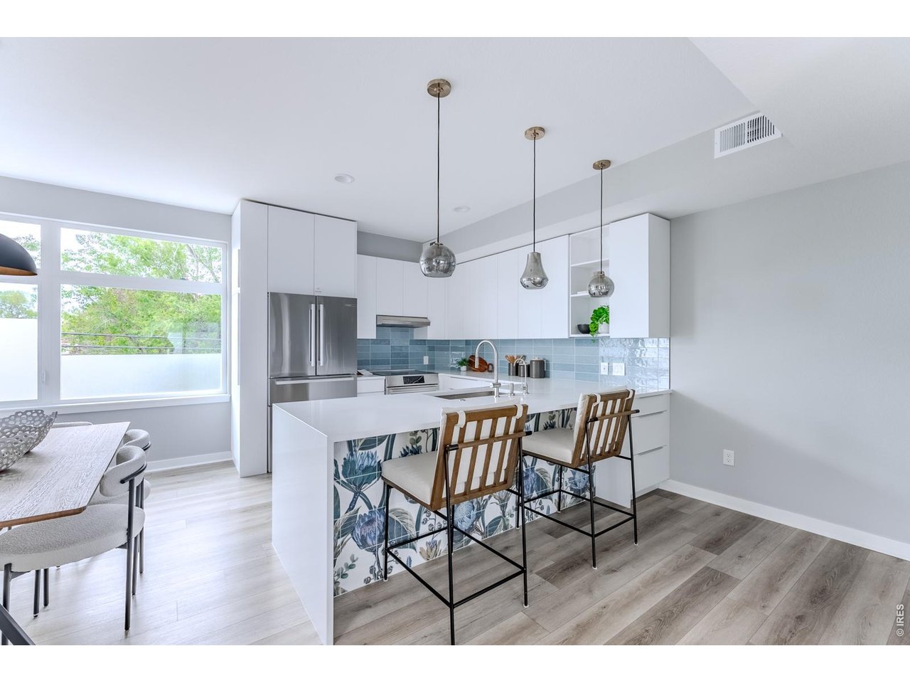 Pendant lighting hovers like jewelry above the space, casting a soft glow that highlights the whimsical custom tile mural adorning the peninsula-an unexpected moment of artistry inspired by the character of the neighborhood it calls home.