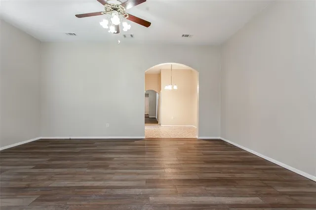 a view of an empty room with wooden floor and a ceiling fan